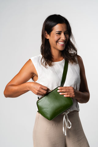 Model is placing a product in the Coneli Fanny Pack bag in color green and is smiling