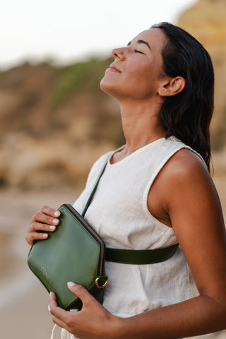 Model in nature, relaxed and sun on her face, wearing the Coneli Fanny Pack green as Cross-Over bag on the beach